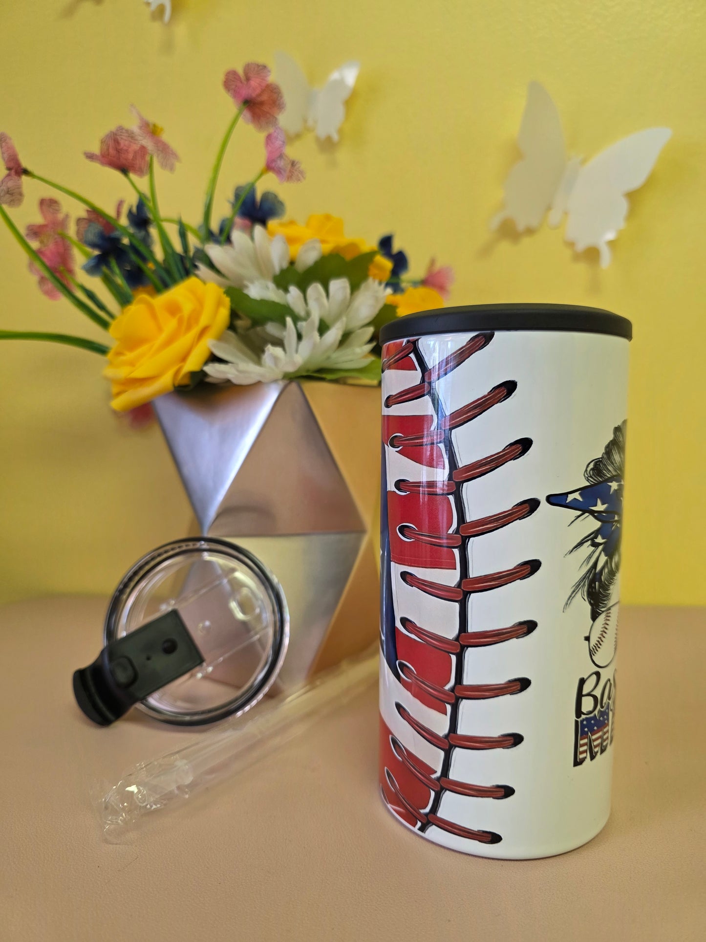 Insulated 4‑in‑1 stainless steel tumbler with baseball‑themed American flag design, shown with lid, straw, and floral arrangement