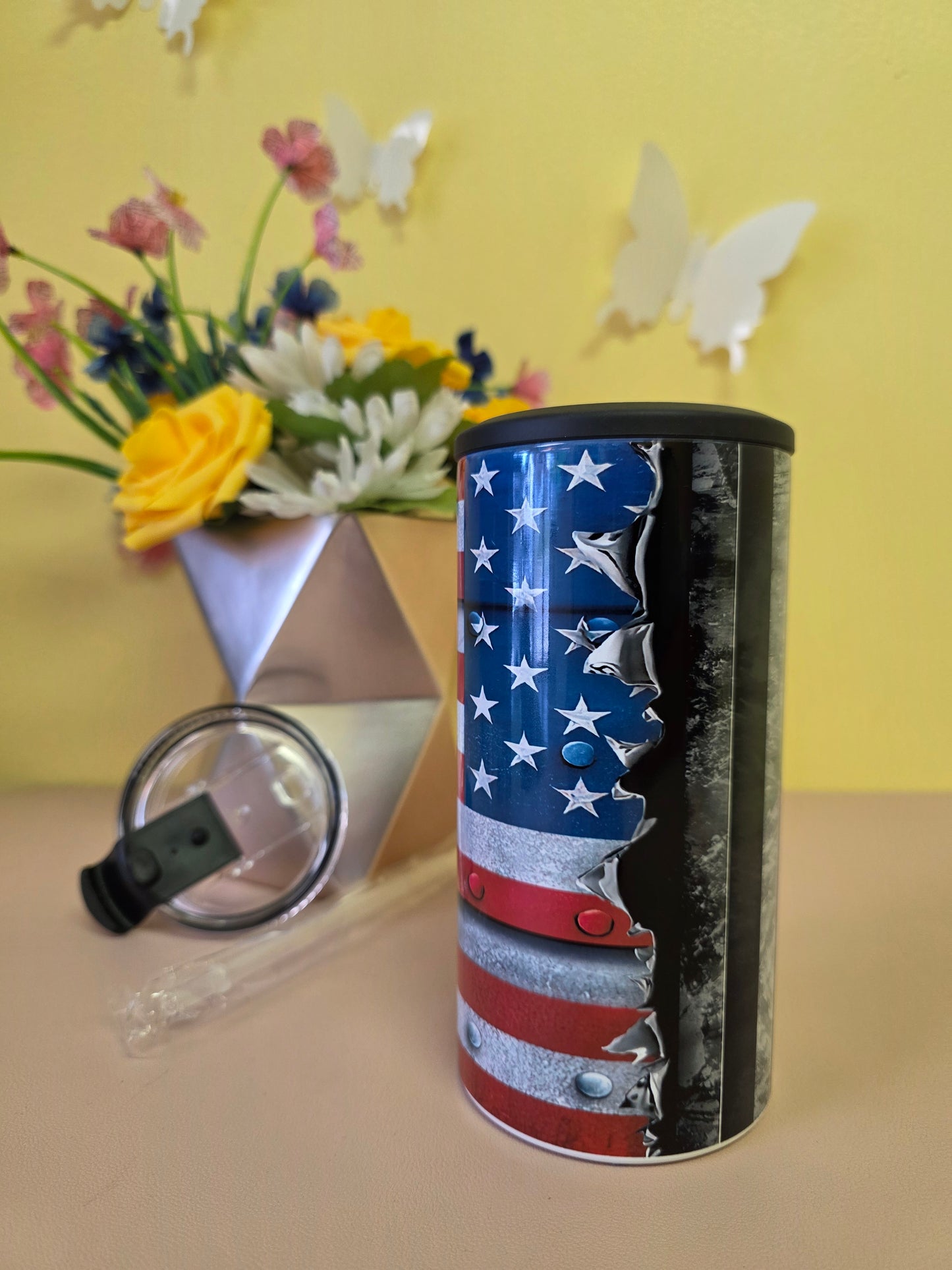 Insulated 4‑in‑1 stainless steel tumbler featuring torn‑metal American flag design, shown with lid and floral arrangement