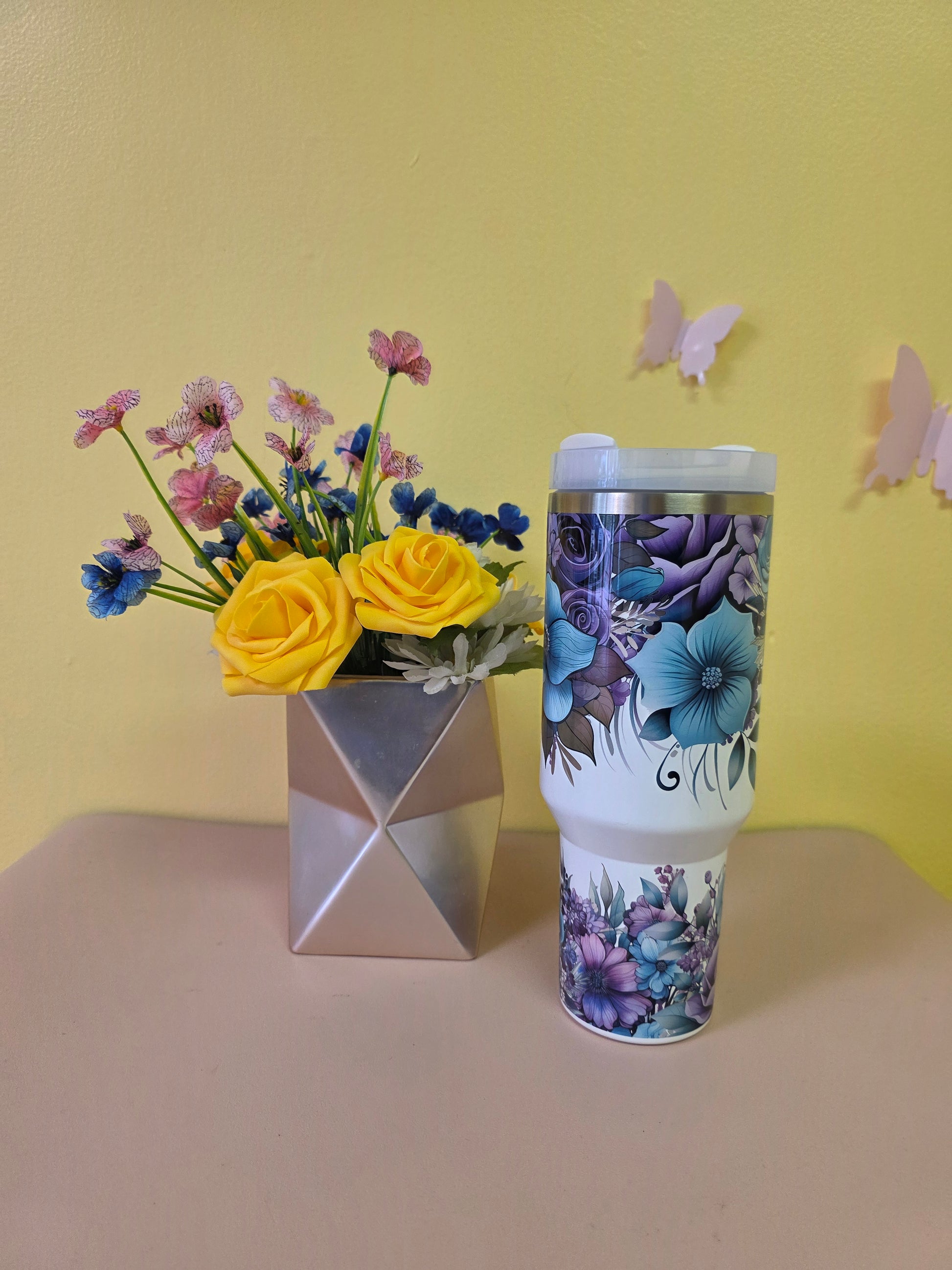 Floral-patterned bottle with a small bouquet of flowers on a yellow surface