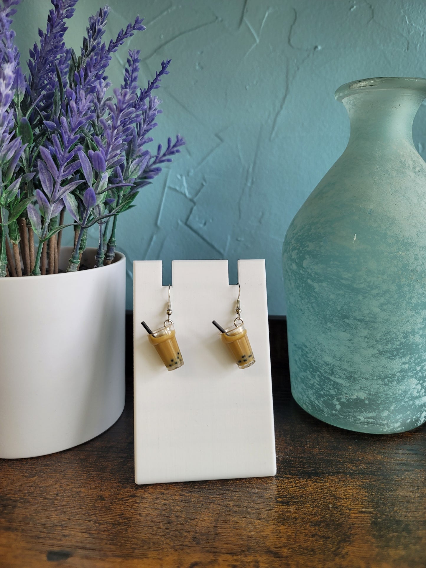 Pair of wooden earrings on a white card with a vase and lavender in the background.