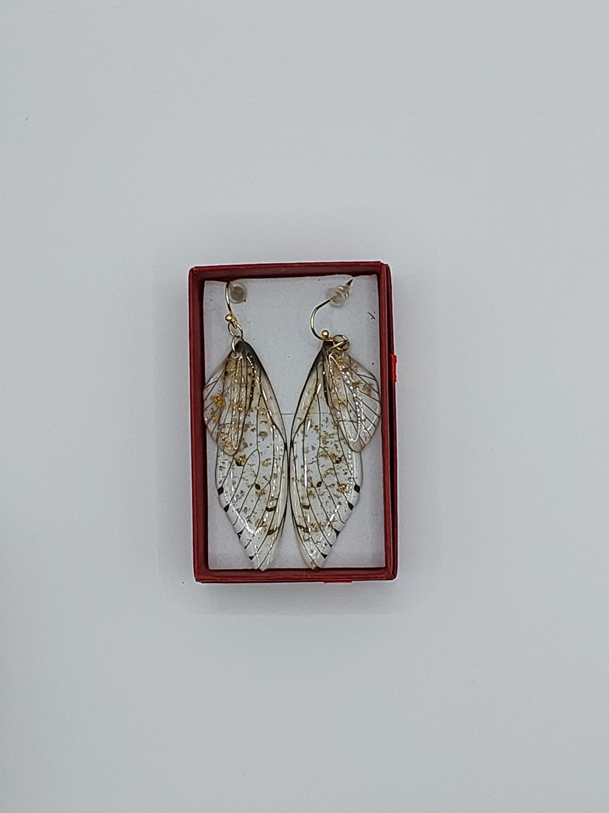 A pair of butterfly wing earrings with gold flecks displayed in a red frame against a white background