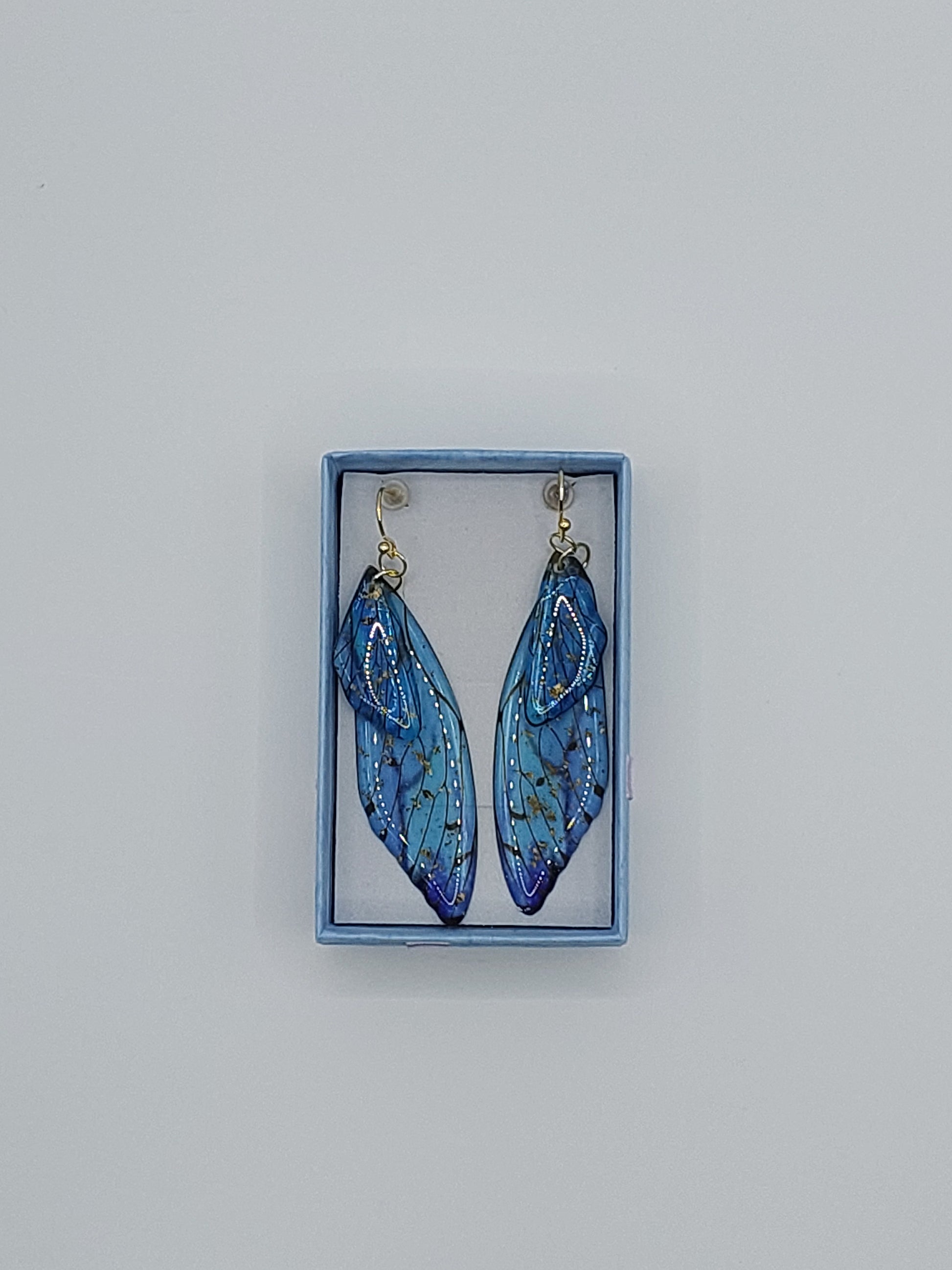 A pair of aqua blue butterfly wing earrings with gold flecks, presented in a small blue box.