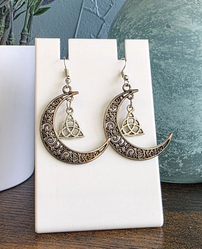 Pair of crescent moon earrings with intricate designs on a white stand.