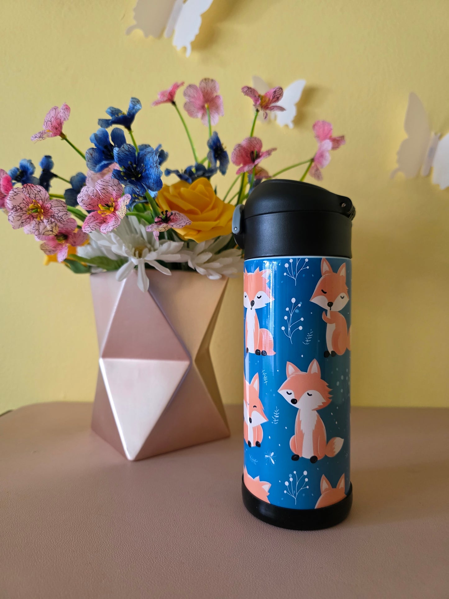 Thermos with fox design on a yellow surface with flowers