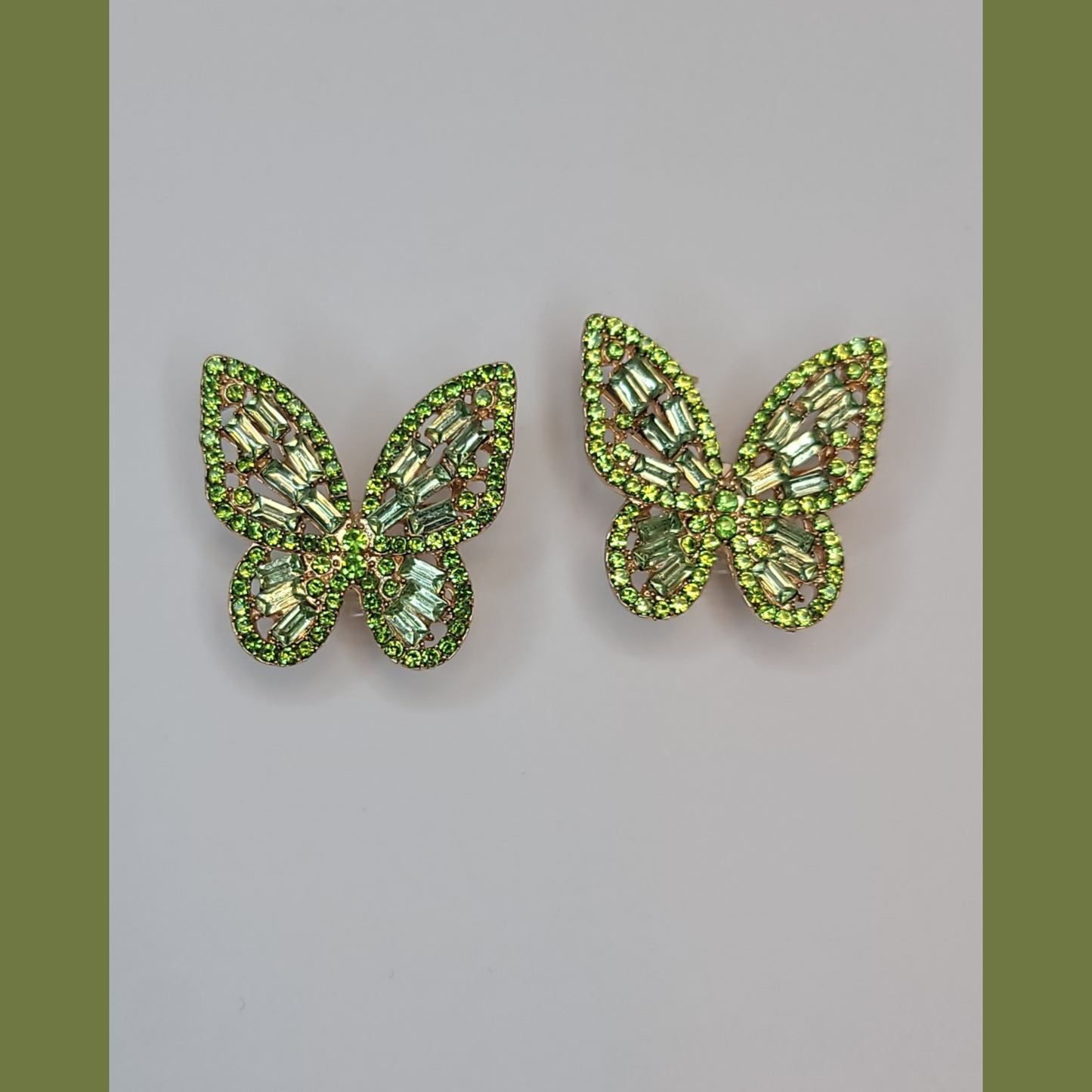 A pair of blue butterfly earrings with purple beads displayed on a white stand, with a lavender plant and a blue vase in the background.