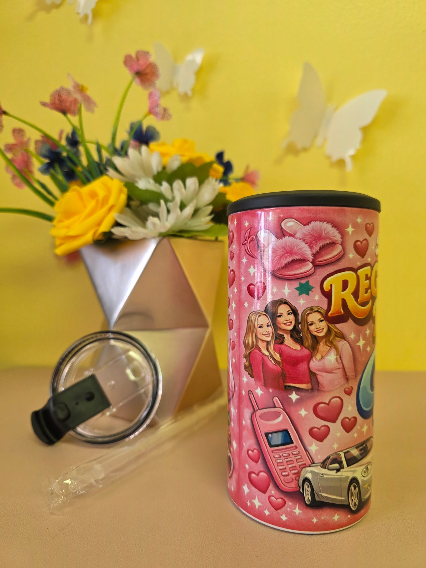 Pink insulated stainless steel tumbler with ‘I’m not a regular mom I’m a cool mom’ design, clear lid, straw, and floral background decor