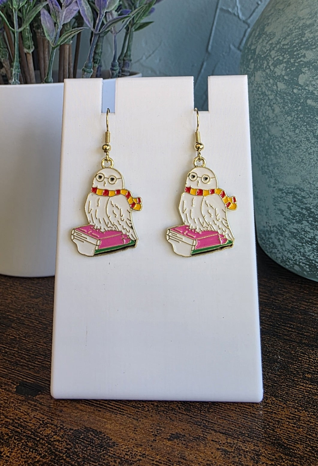 Harry Potter earrings with Hedwig sitting on books with a Gryffindor scarf.