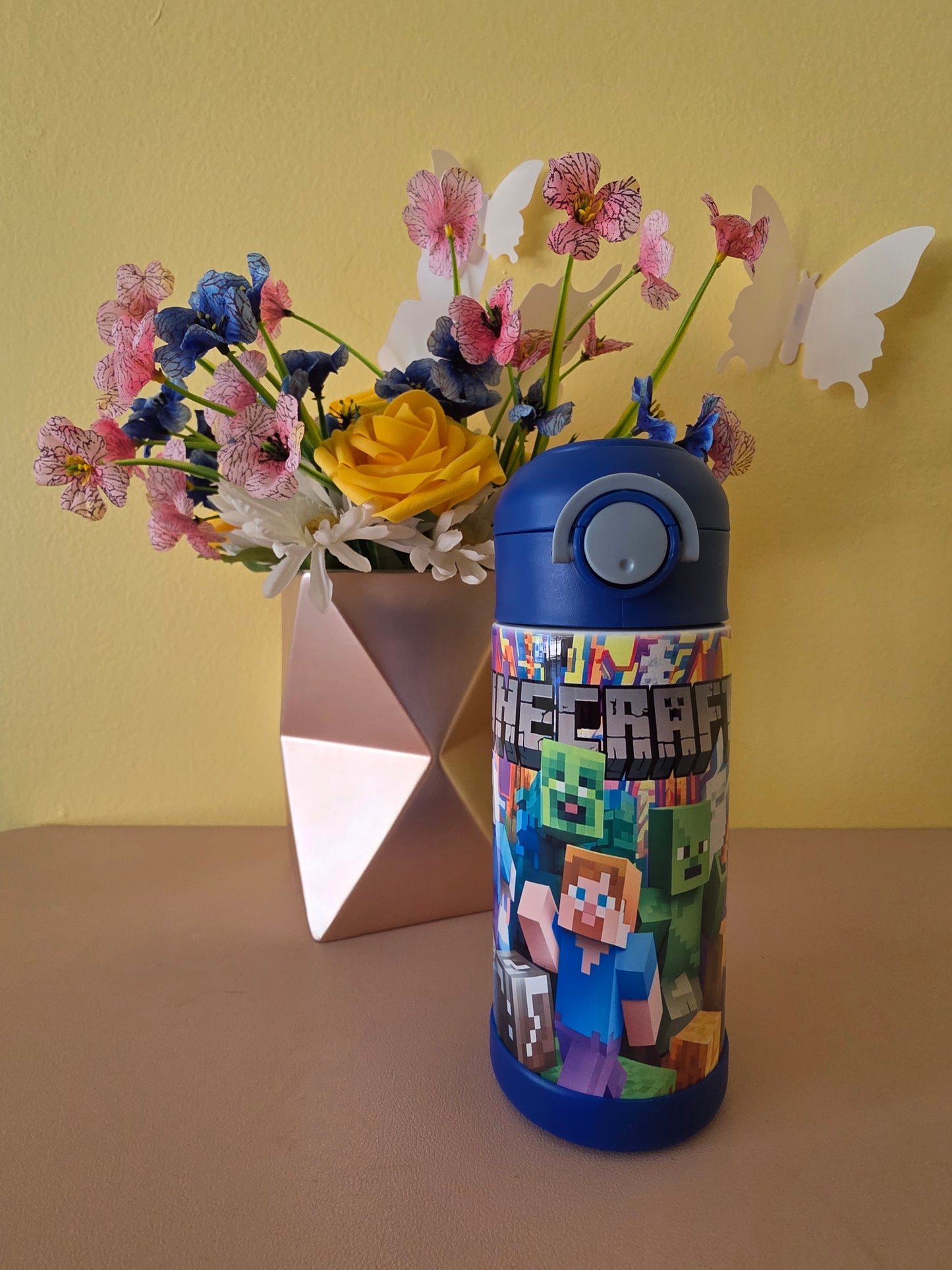 Minecraft stainless steel water bottle for kids on a table with flowers in the background.