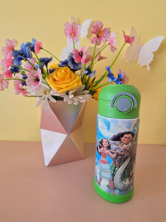Moana and Maui Tumbler on a table with flowers in the background.