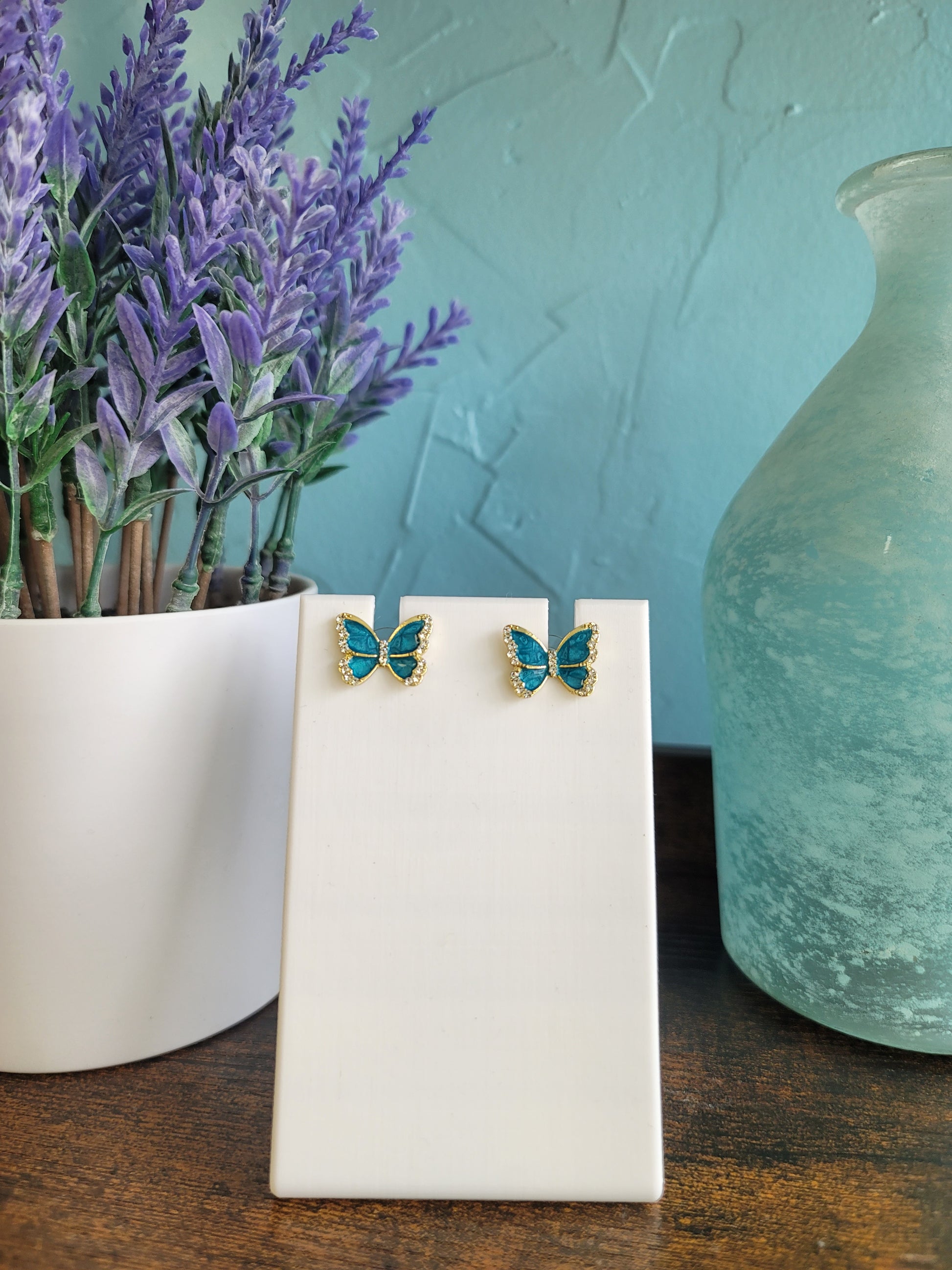 Butterfly-shaped earrings on a white stand with a blurred natural background.
