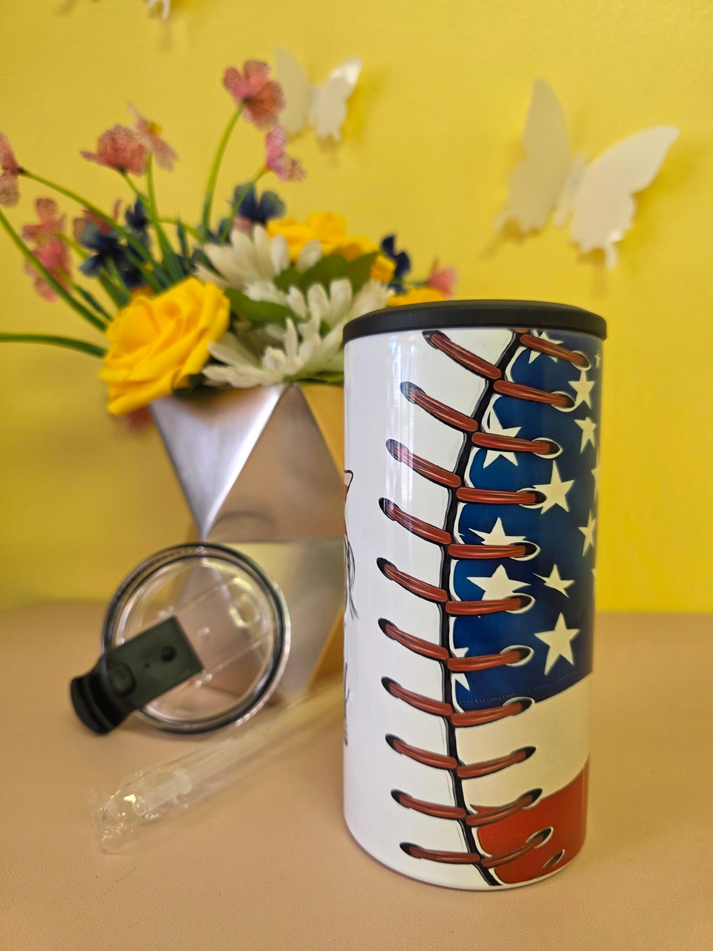Insulated 4‑in‑1 stainless steel tumbler with baseball‑themed American flag design, shown with lid, straw, and floral arrangement