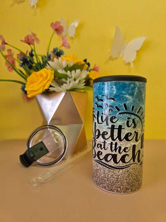 Insulated 4‑in‑1 stainless steel tumbler with sandy beach, ocean waves, and palm tree design, shown with lid, straw, and decorative flowers