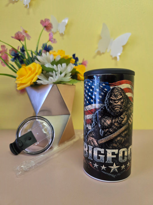 Black insulated stainless-steel tumbler with eagle and American flag artwork, shown with lid, straw, and floral background
