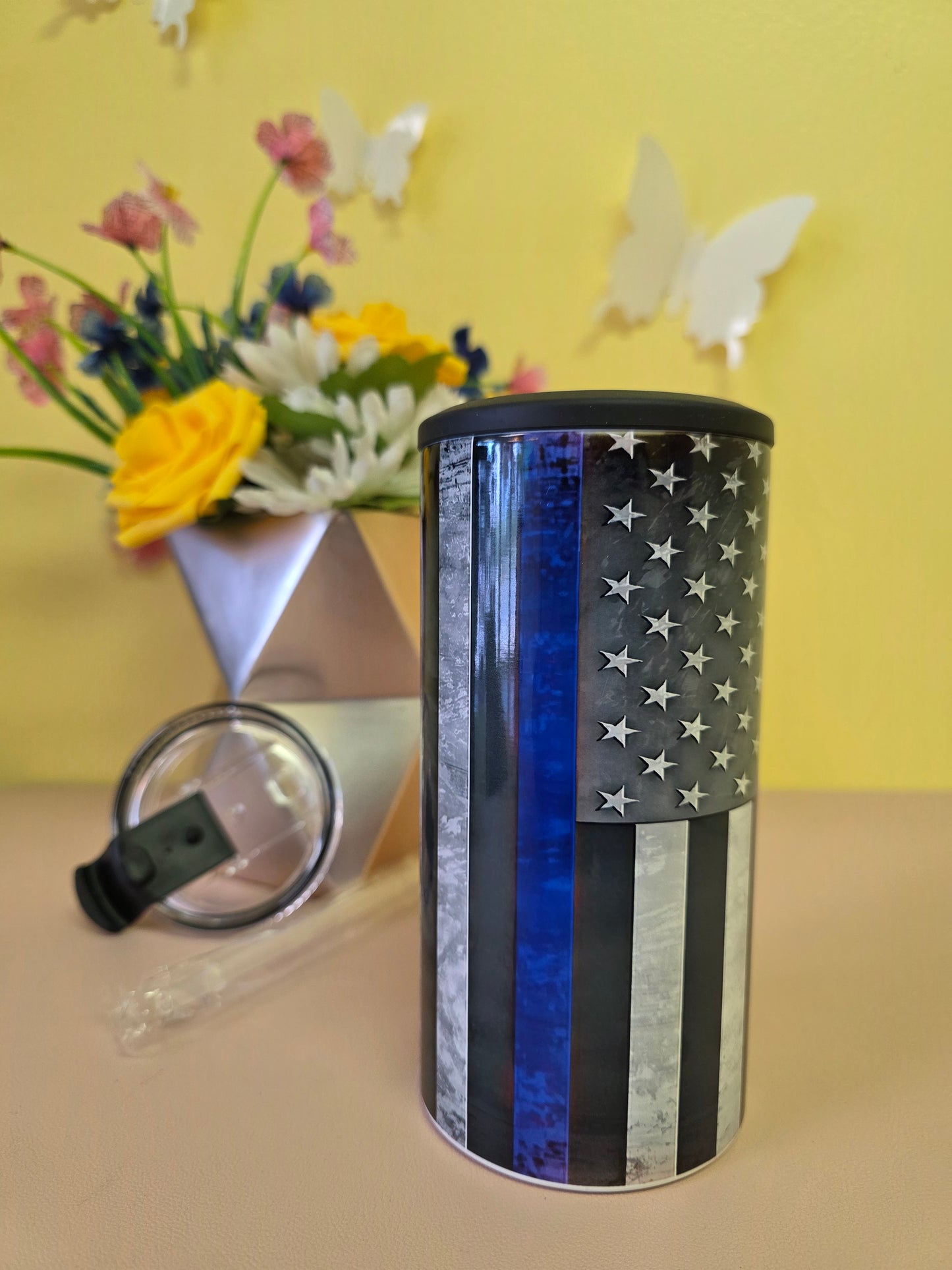Insulated 4‑in‑1 stainless steel tumbler featuring torn‑metal American flag design, shown with lid and floral arrangement