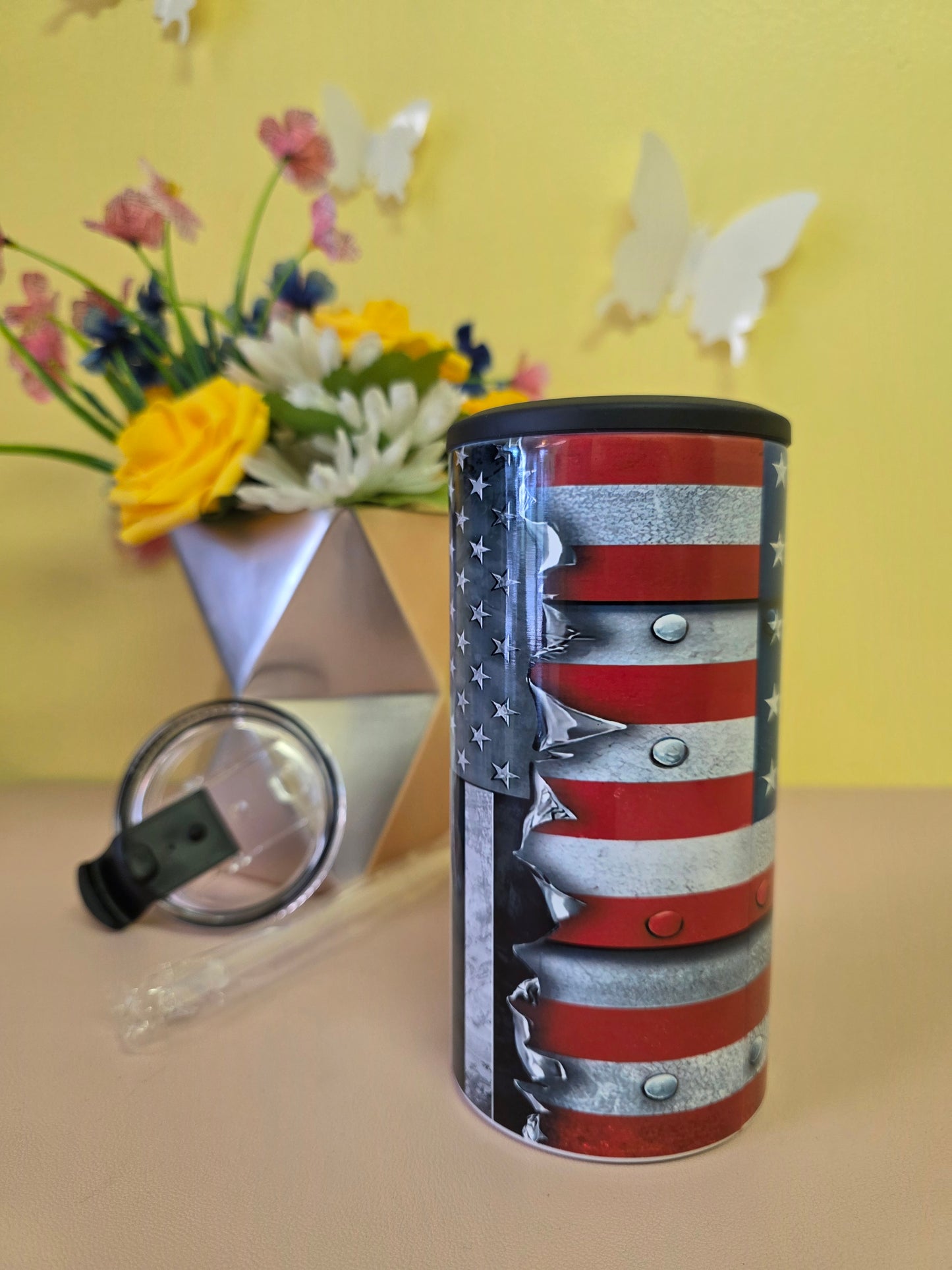 Insulated 4‑in‑1 stainless steel tumbler featuring torn‑metal American flag design, shown with lid and floral arrangement