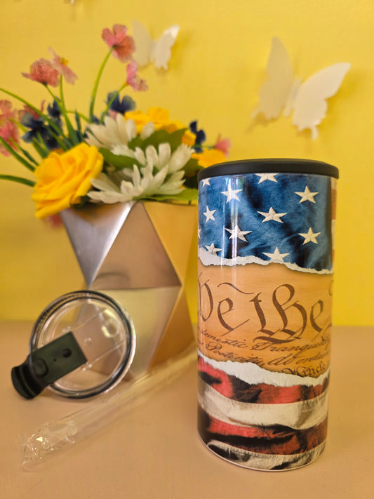 Insulated 4‑in‑1 stainless steel tumbler with U.S. Constitution text and American flag design, shown with lid, straw, and floral arrangement