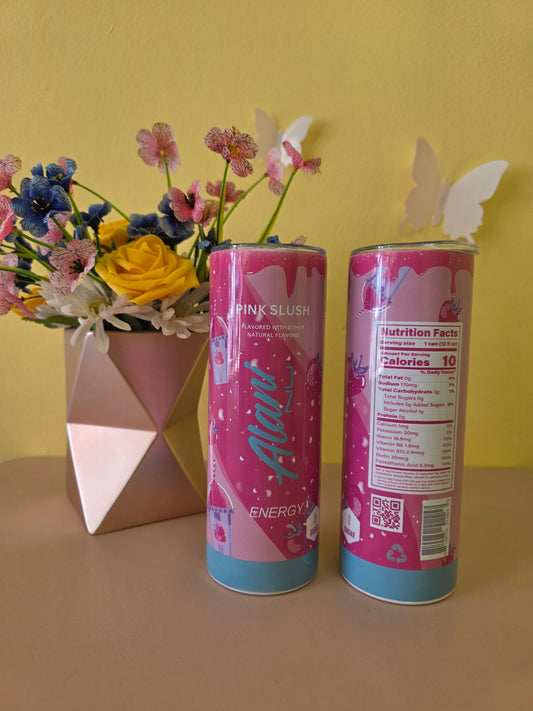 Two pink energy drink cans on a yellow surface with flowers and a box. Alani Pink Slush