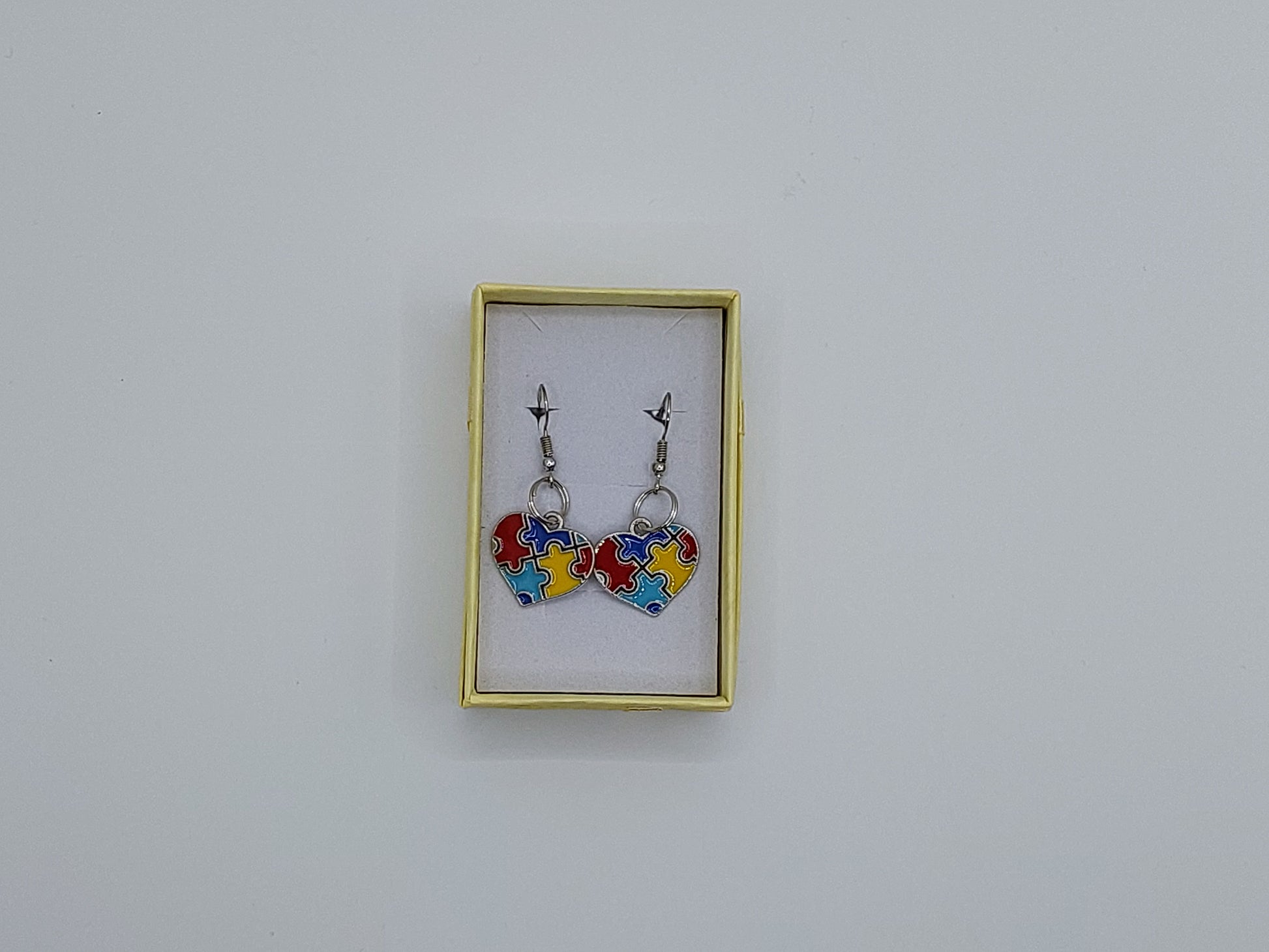 A small pair of earrings with autism puzzle piece hearts and silver finish.