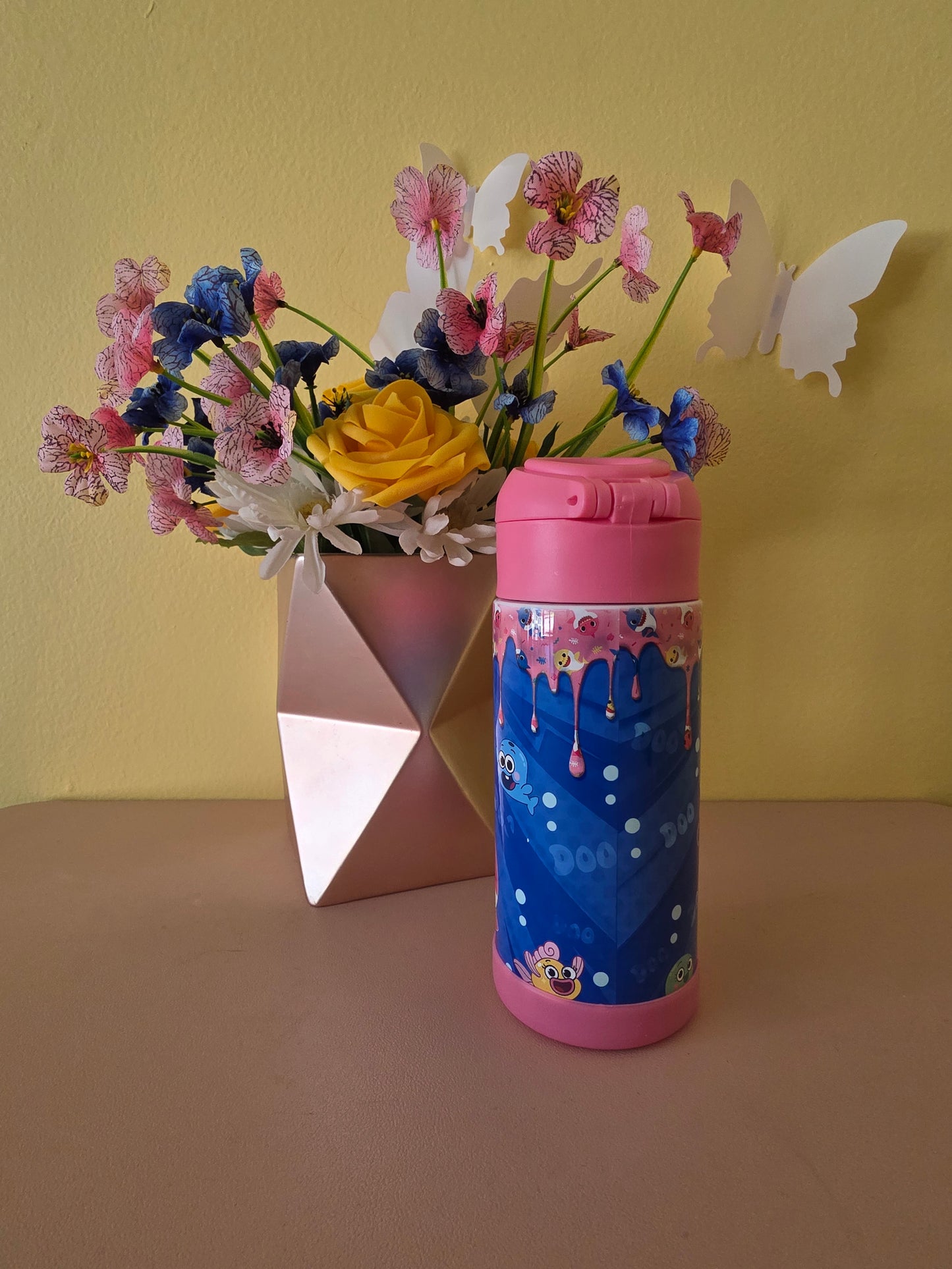 Baby Shark kids water bottle tumbler on a table with flowers in the background