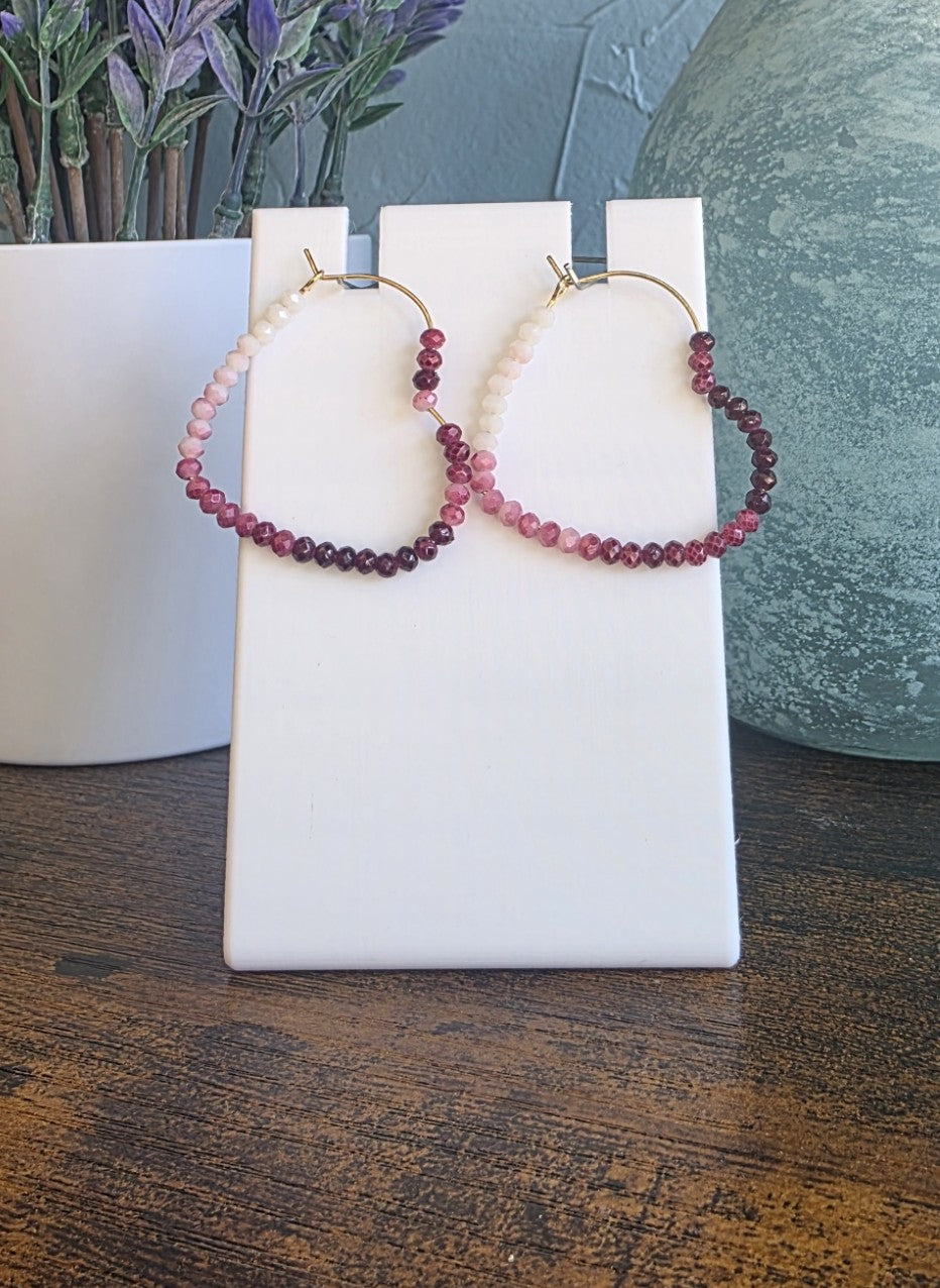 Beaded heart hoop earrings on a white card with a plant and vase in the background