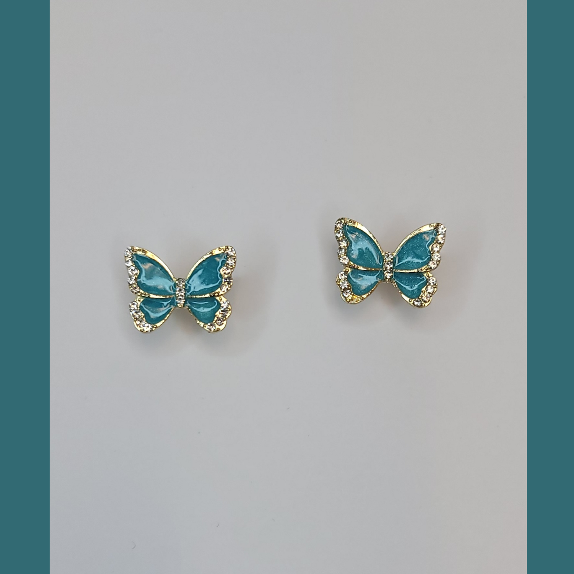A pair of blue butterfly earrings with purple beads displayed on a white stand, with a lavender plant and a blue vase in the background.