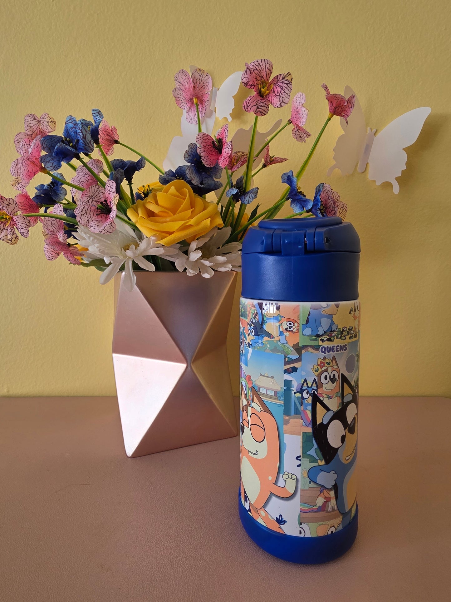 Bluey tumbler water bottle with lid and straw on a table with flowers in the background 