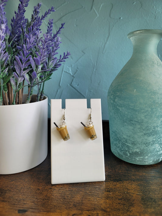 Pair of wooden earrings on a white card with a vase and lavender in the background.