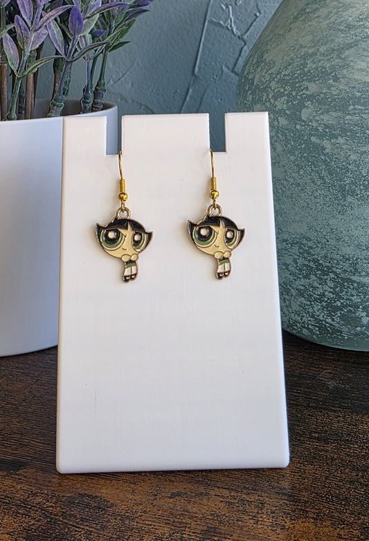 Pair of gold earrings on a white card with a plant and vase in the background