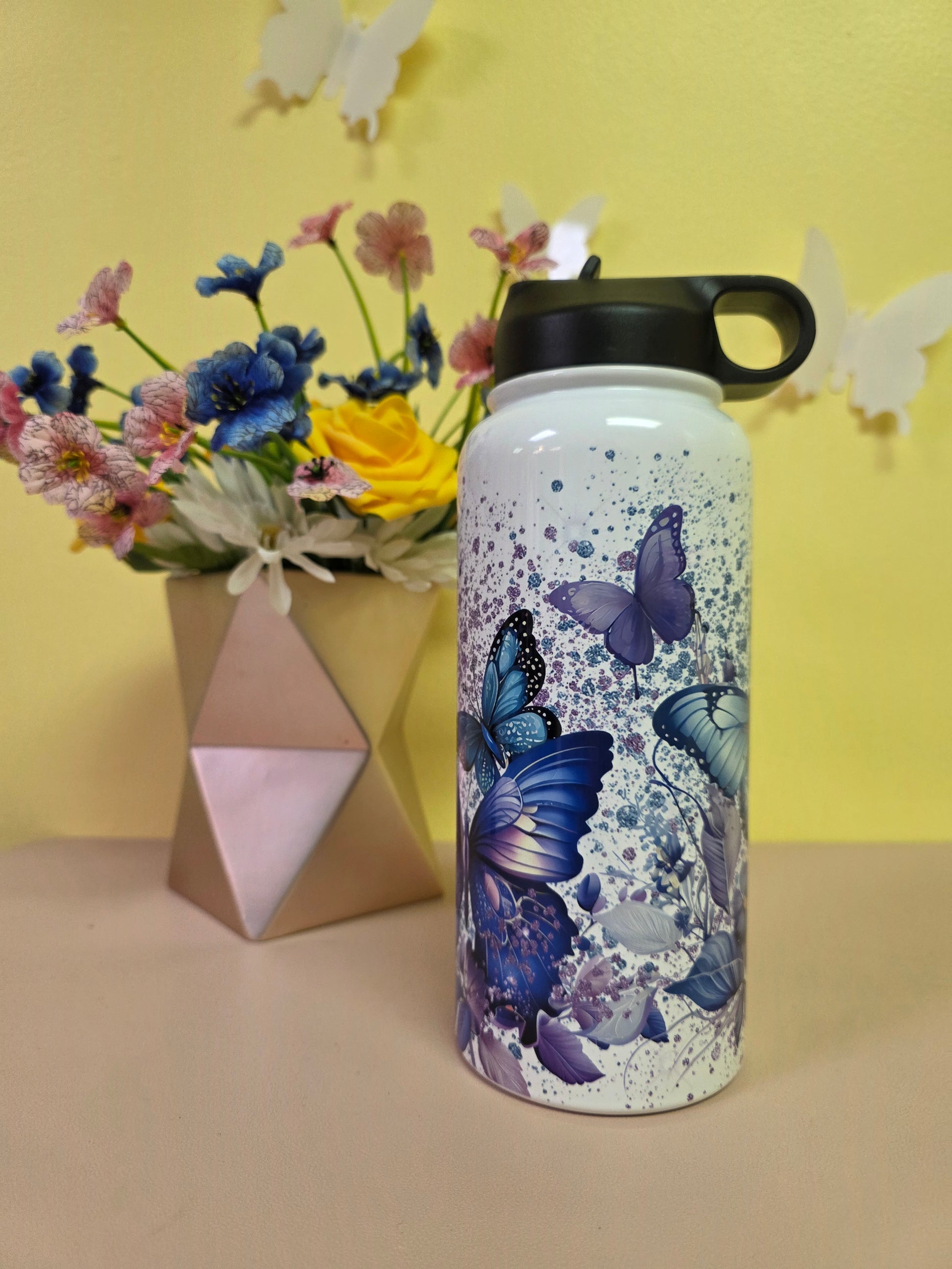 White water bottle with butterfly design on a yellow background with flowers and geometric shapes.