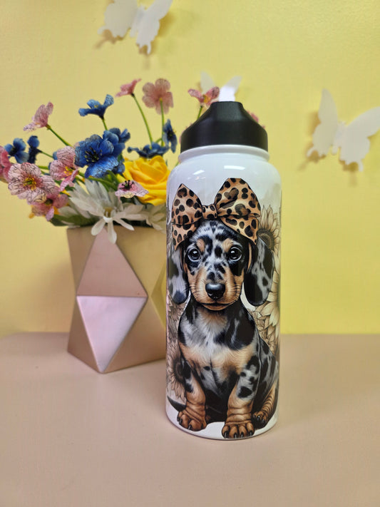 Tumbler with a dachshund design on a yellow surface with flowers and a box.