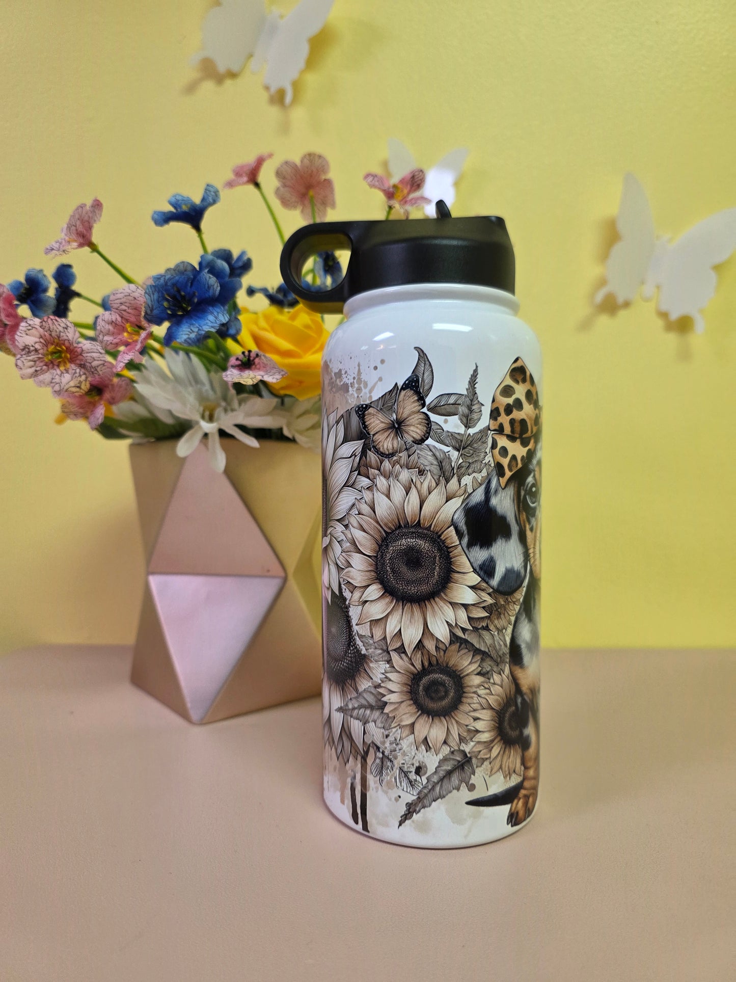 Floral-patterned water bottle on a yellow surface with flowers and a geometric object.