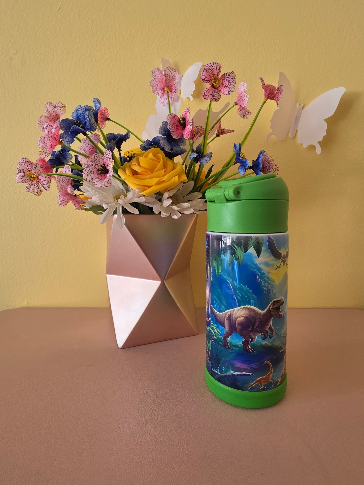Dinosaurs print stainless steel water bottle for kids on a table with flowers in the background. 