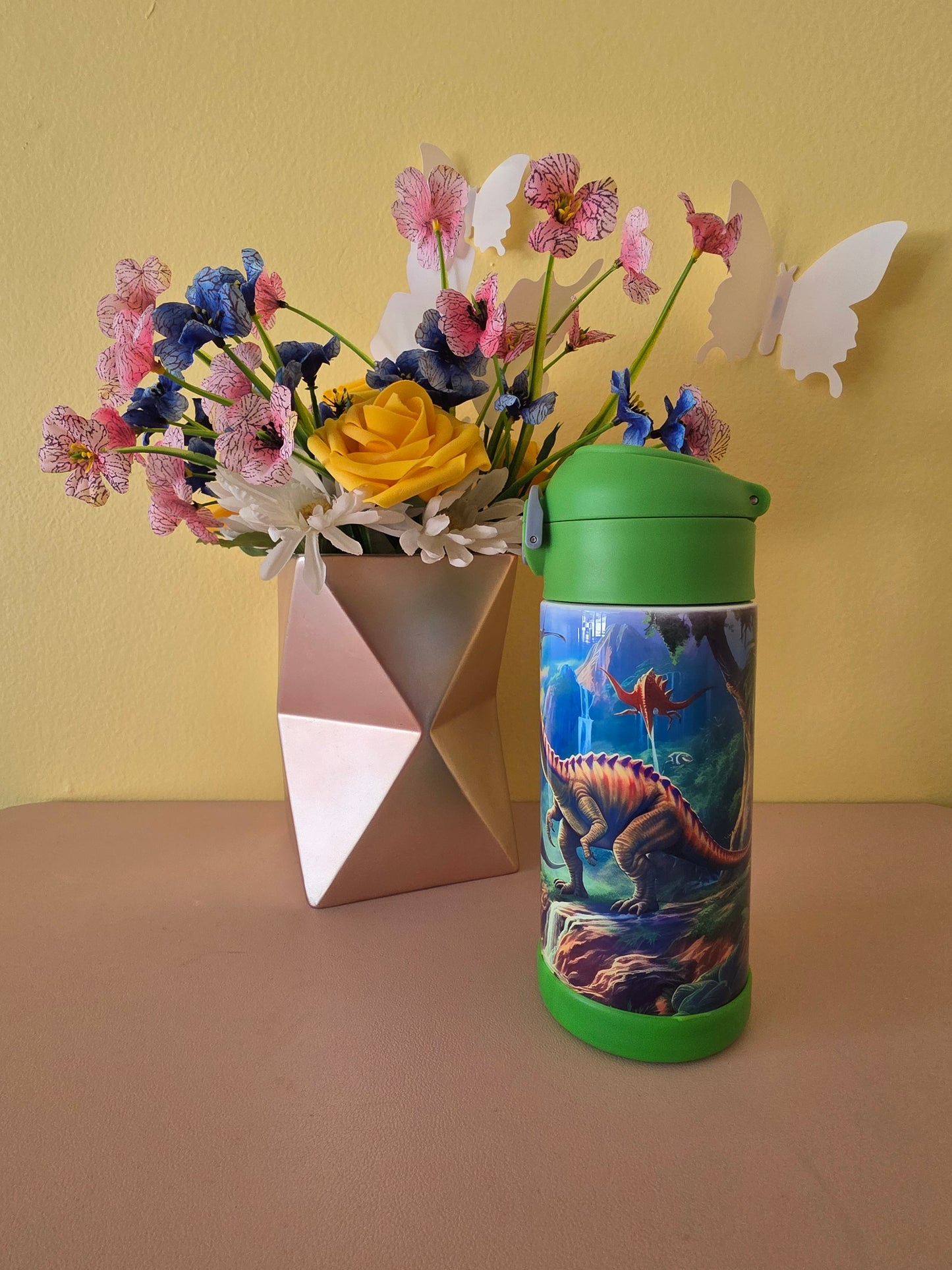 Dinosaurs print stainless steel water bottle for kids on a table with flowers in the background. 