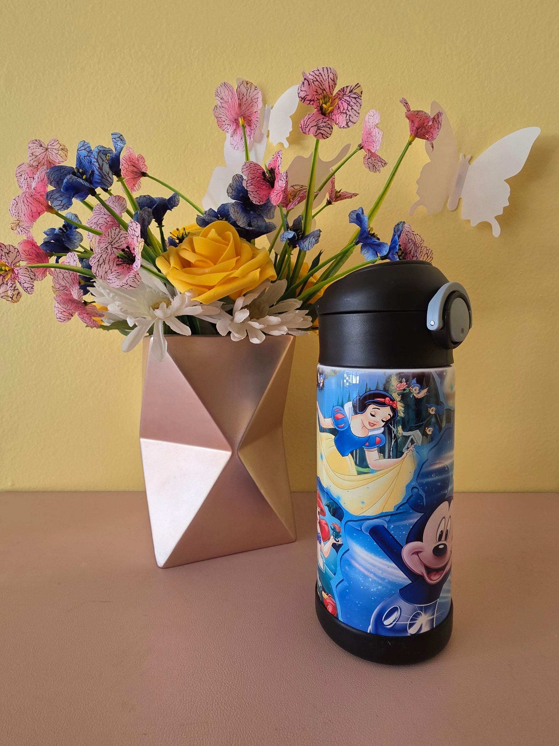 Disney character tumbler on a table with flowers in the background. 