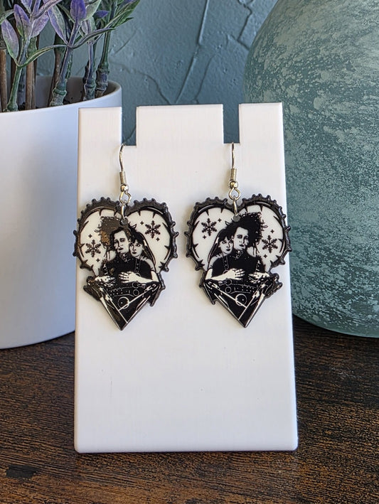 Heart-shaped earrings with a design of two people holding embracing on a white card.