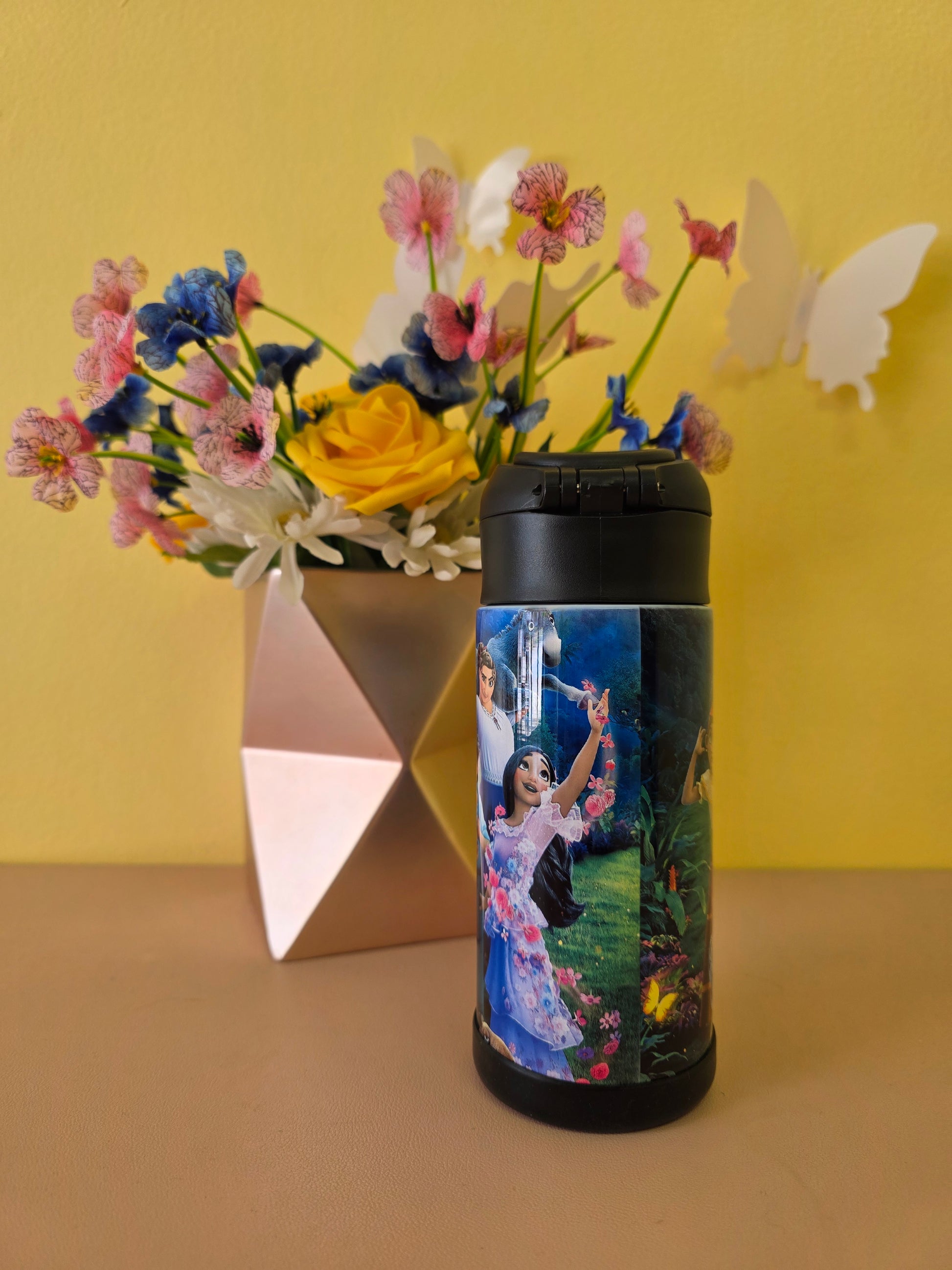 Floral arrangement with a cylindrical container featuring artistic design on a yellow background