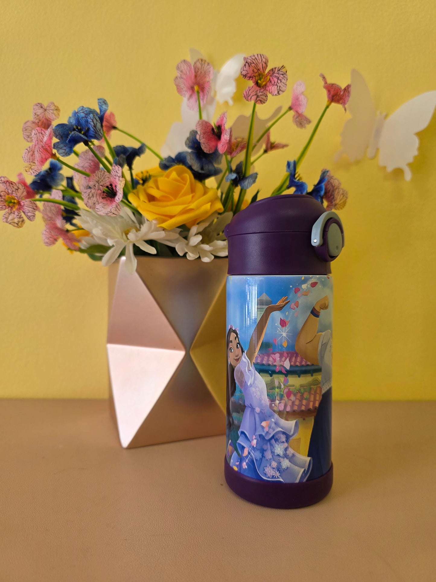 Tumbler with a colorful design on a yellow surface next to a bouquet of flowers