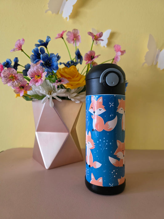 Thermos with fox design next to a bouquet of flowers on a yellow background