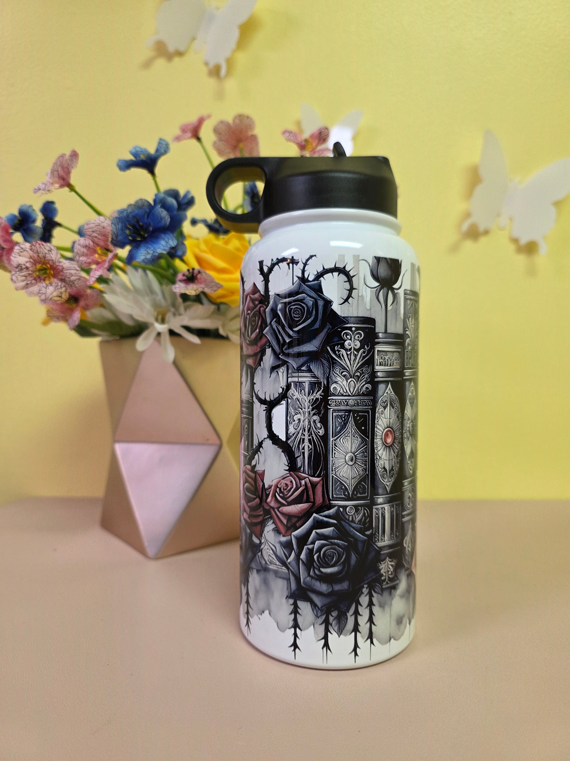 Water bottle with black and white design on a yellow surface with flowers and a box.