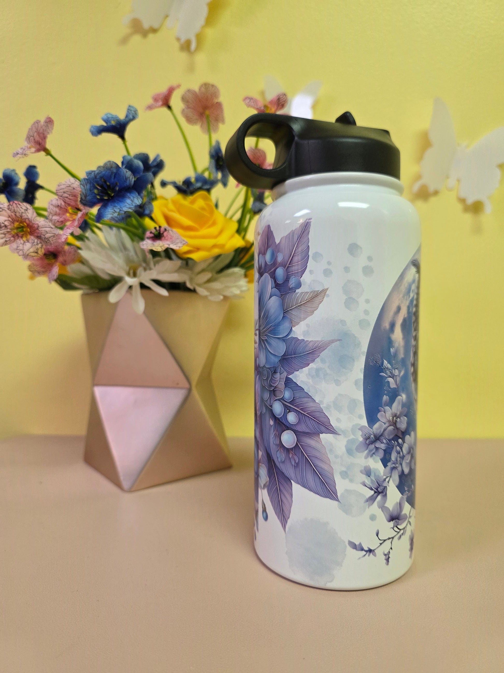 Floral-patterned tumbler on a yellow surface with flowers and geometric shapes.