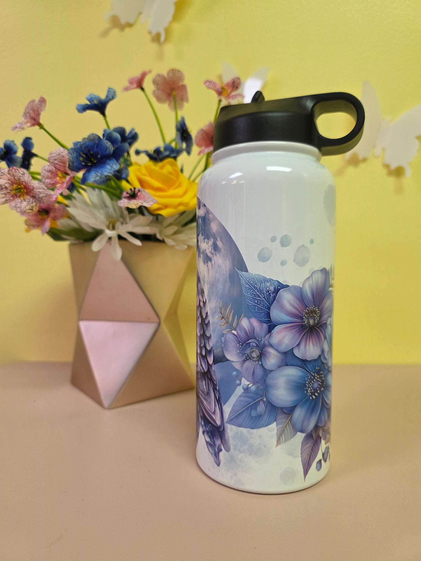 Floral-patterned water bottle on a yellow surface with flowers and a geometric object.