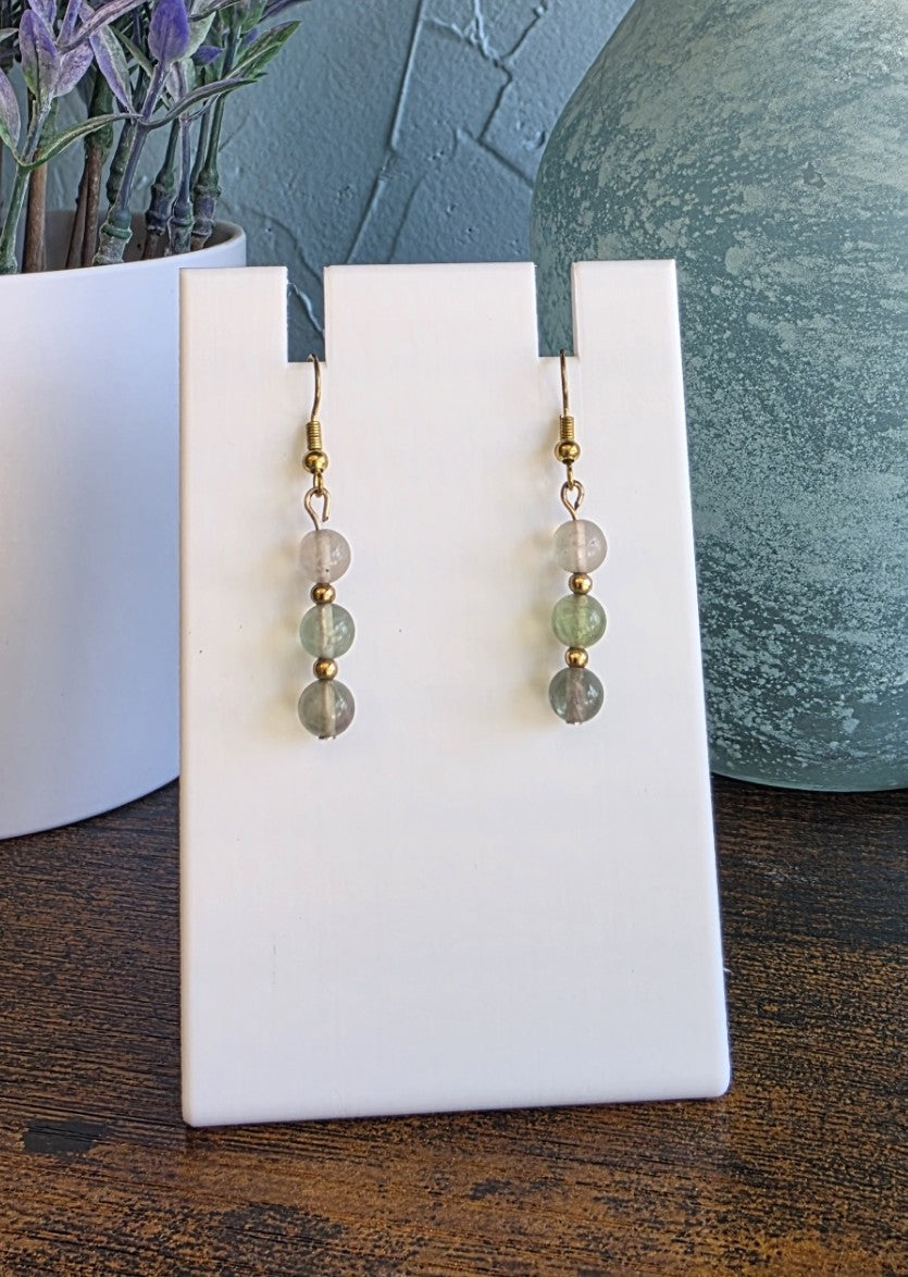 Pair of green beaded earrings on a white card with a blurred background