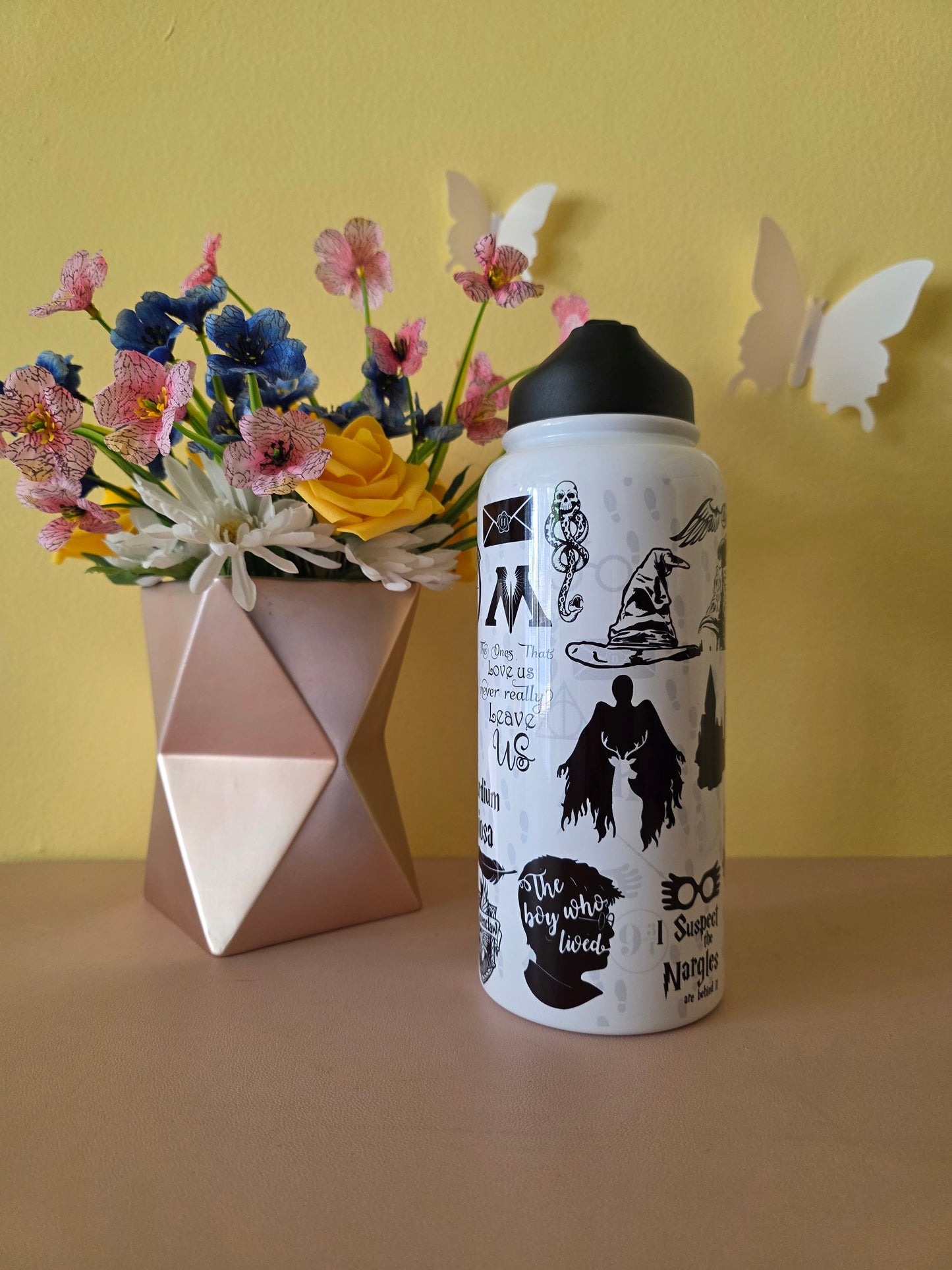 Harry Potter themed stainless steel water bottle on a table with yellow background