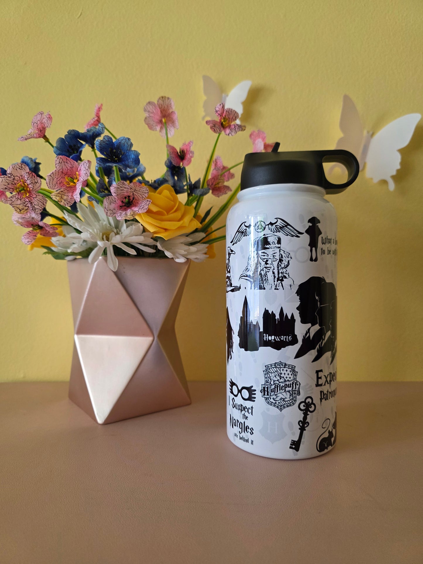 Harry Potter themed stainless steel water bottle on a table with yellow background
