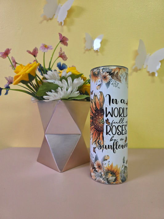 Decorative cylindrical container with floral design and text, placed on a yellow surface with flowers and a pink triangle.