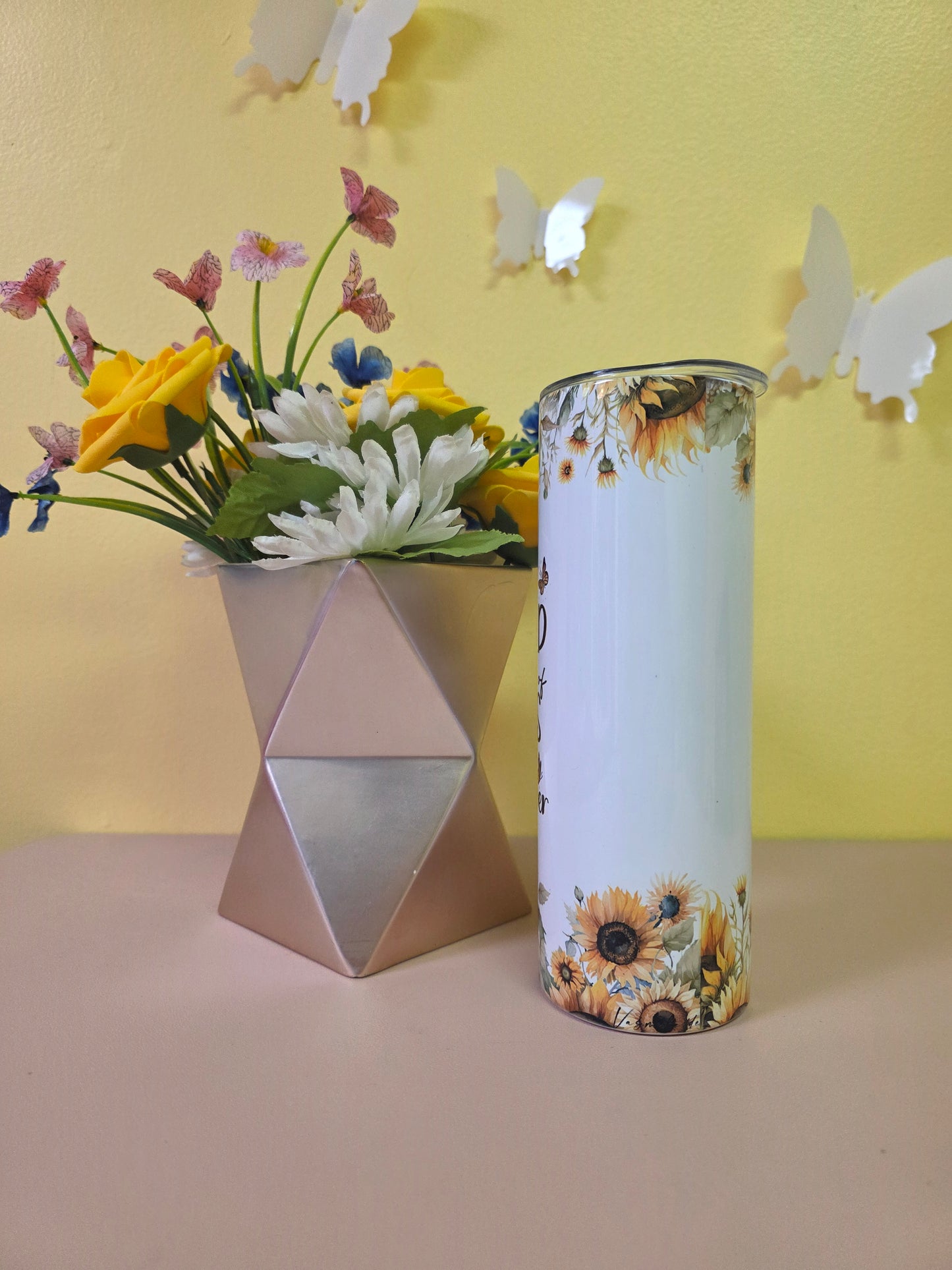 Decorative cylindrical object with sunflower design on a yellow surface with flowers and butterflies.
