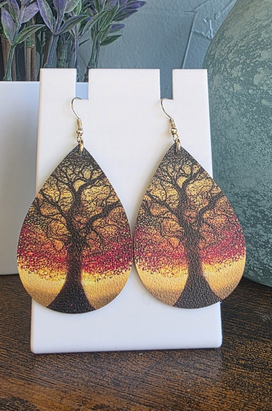 Teardrop-shaped earrings with tree design and sunset colors on a white stand.