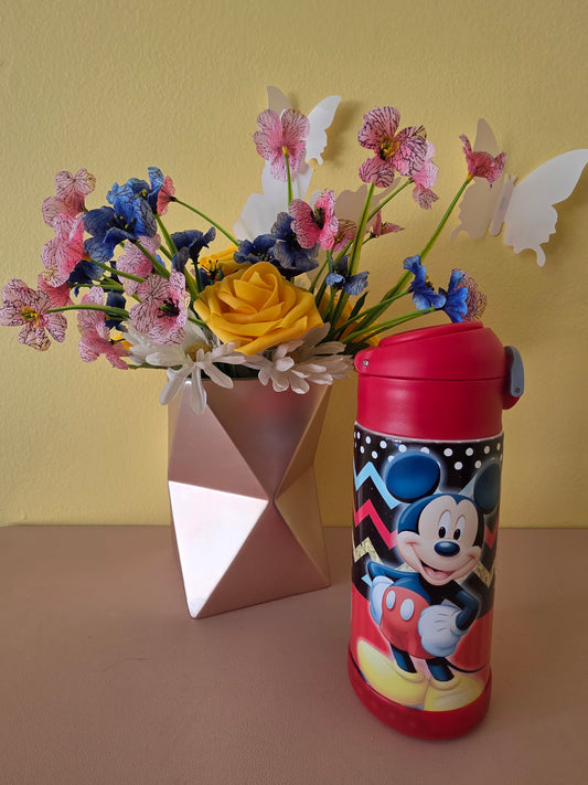 Mickey Mouse tumbler for kids on a table with flowers in the background. 
