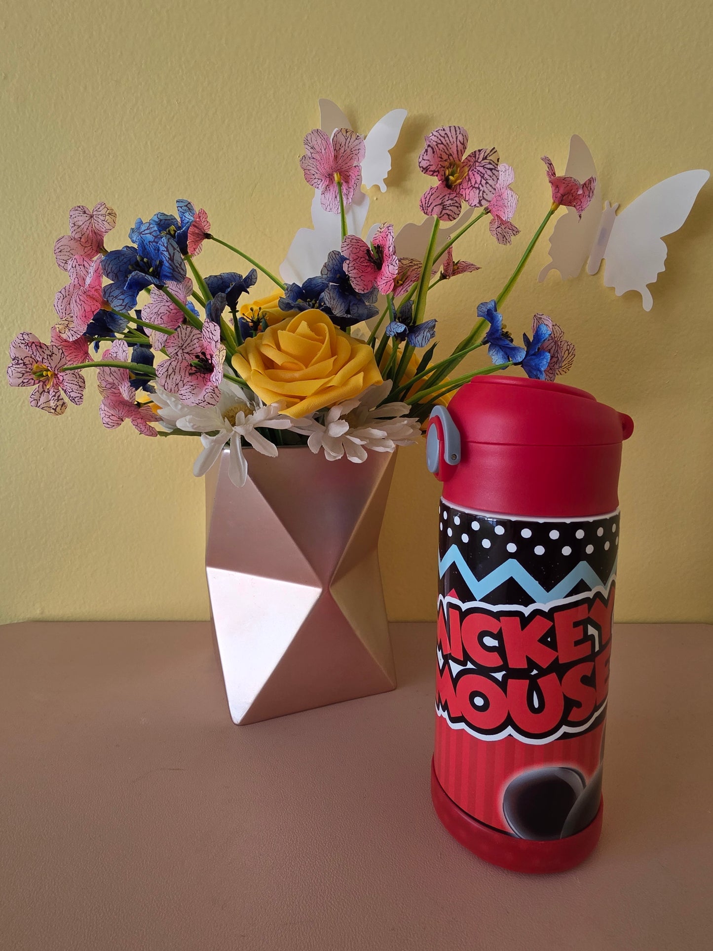 Mickey Mouse tumbler for kids on a table with flowers in the background. 