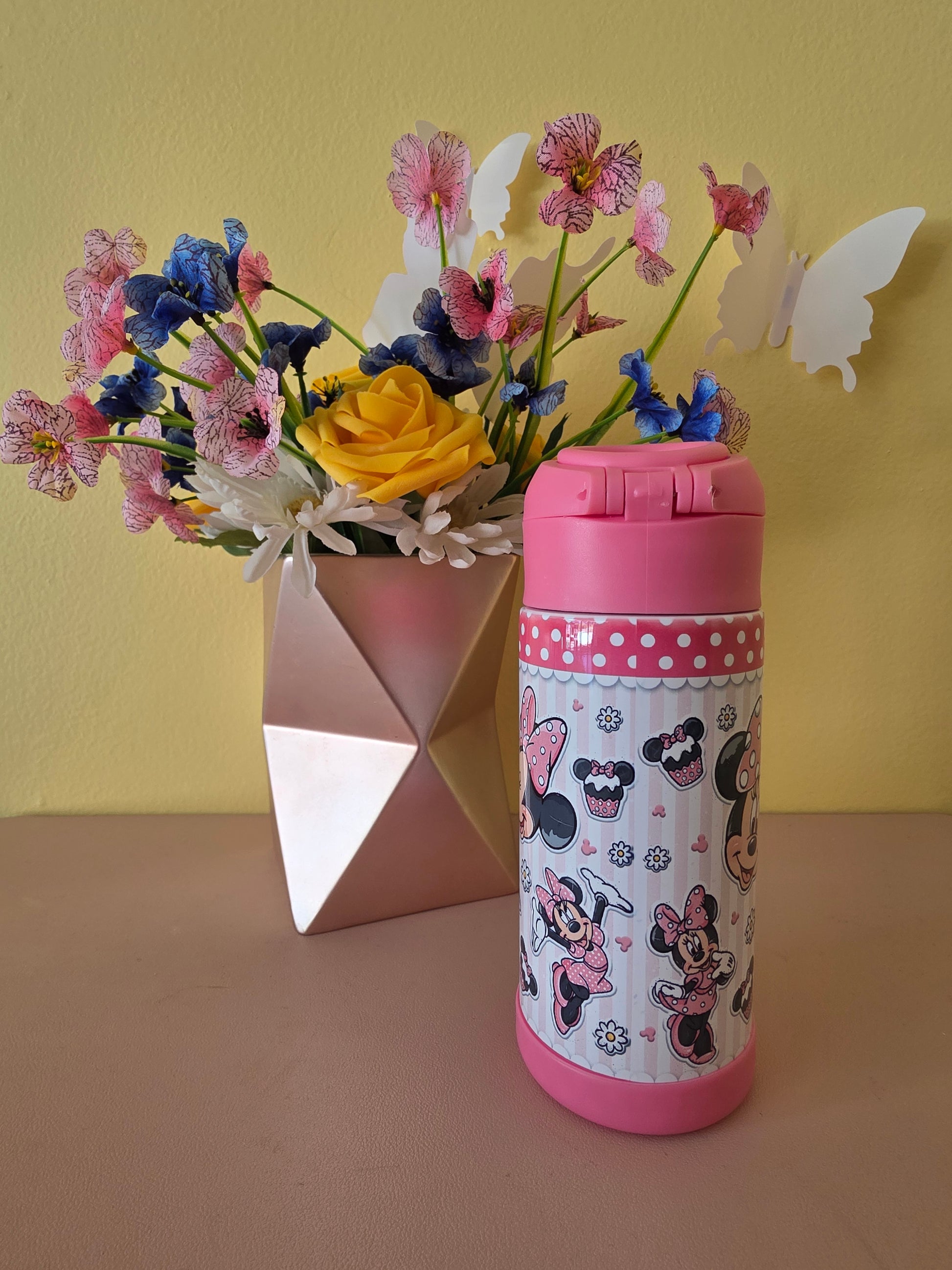 Pink Minnie Mouse tumbler for kids ion a table with flowers in the background. 